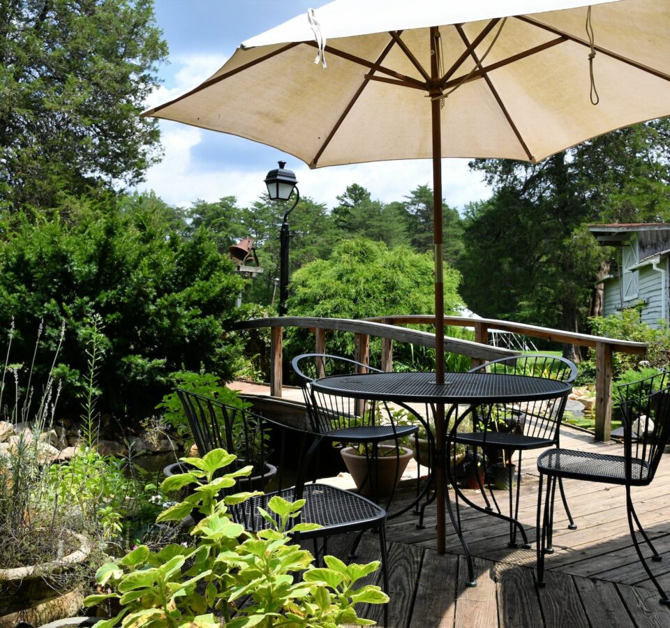 A cozy backyard outdoor living space with a table and umbrella on a deck next to a pond landscaping