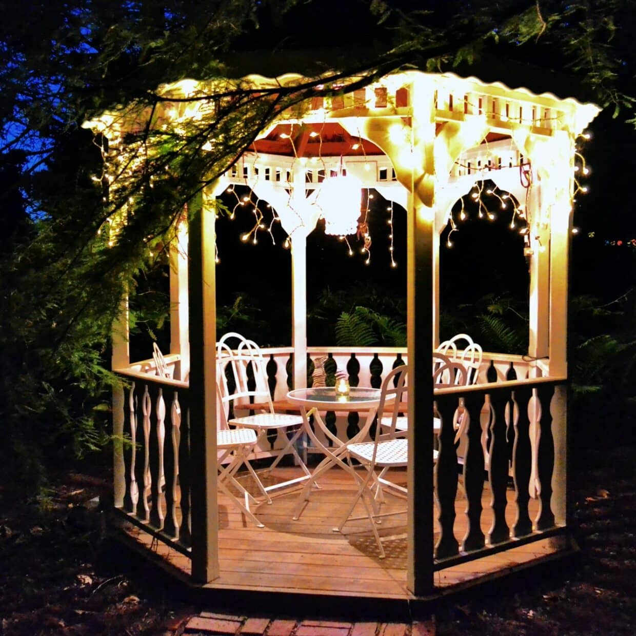 Gazebo in a garden at night with lights, a table and chairs